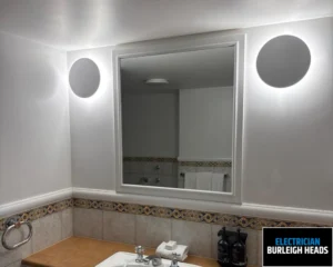 Modern bathroom with a white sink, wooden countertop, mirror, and round wall light.